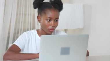 Ciddi bir Afro-Amerikan kadın. Laptop üzerinde çalışıyor. Ofiste masada oturuyor. Serbest iş, dijital göçebeler yaşam tarzı kavramı. İçerik yaratan odaklanmış kız blog yazarı.