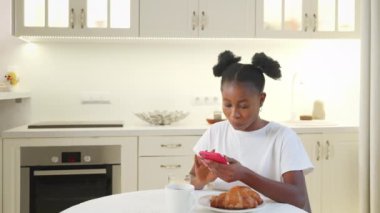 Ev mutfağında akıllı telefonu olan siyahi kadın, cep telefonuyla internette sörf yapan Afrikalı Amerikalı genç bayan, sosyal medya bağımlılığı, mobil uygulamadan online alışveriş.