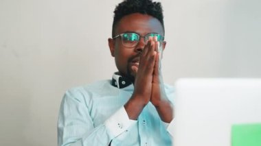 Dizüstü bilgisayarda endişeli bir adam ekranda dua jesti ile bekliyor. Memnun Afro-Amerikalı adam, olumlu cevap yazarak seviniyor. İnternette çalışmak, sıkı müzakere kavramı.