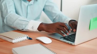 Asık suratlı Afro-Amerikan programcı dizüstü bilgisayarda yazı yazıyor. Masada oturan ekrana bakıyor. Mavi gömlekli adam çalışıyor. İşyerinde odaklanmış işkolik. Ofis hayatı.