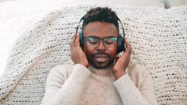 Afro-Amerikan portresi. Kulaklıkla müzik dinleyen rahat bir adam. Kafasını yatakta ritimle hareket ettiriyor. Adam müzik sever, gözlüklü, evde dinlenen favori şarkıların tadını çıkaran biri..