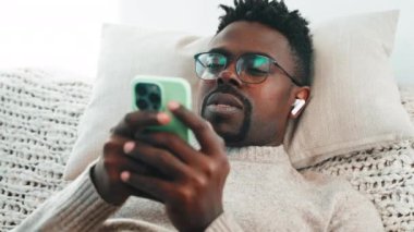 Akıllı telefonlu siyah bir adam hafta sonu ya da tatilde evde dinleniyor, modern akıllı telefonlu yüz ve ellere yakından bakıyor, mobil uygulama kullanıyor ve görüntülü konuşma yapıyor, uzaktan iletişim kuruyor.