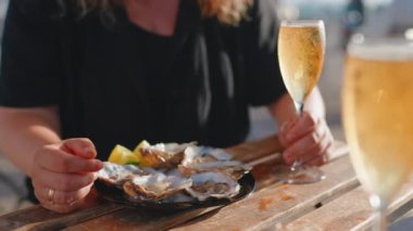 Kadın deniz ürünleri restoranında akşam yemeğinde, tabağında istiridye ve şampanya bardakları, yakın çekim manzarası, yıldönümü kutlaması ya da sahil şeridindeki deniz ürünleri kafede romantik bir buluşma.