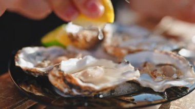 Kadın eli istiridye suyu sıkıyor limon sıkıyor güneşli bir günde restoranda yemek için hazırlanıyor, yakın çekim manzarası var. Yenilebilir taze çiğ deniz ürünleri. Akdeniz mutfağı mutfak konsepti.