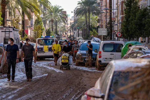 İspanya 'nın Valencia kentinde meydana gelen sel felaketinden sonra gönüllü ve vatandaşlar çamurla dolu bir caddede yol alıyorlar. Maske takarak ve temizlik malzemelerini taşıyarak, enkazı temizlemek ve bölgeyi eski haline getirmek için birlikte çalışıyorlar.. 