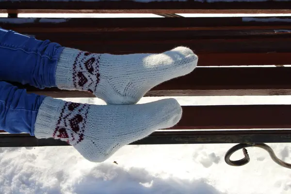woman wearing knitted socks sitting on a bench in the park.