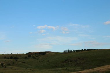 Yazın manzarada tepeler ve arkasında bulutlar olan mavi gökyüzü..