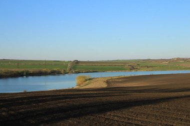 Nehir, ağaçlar, çimenler ve mavi gökyüzüyle manzara