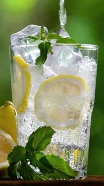 Bardağa buz, limon dilimleri ve tahta bir tahtanın üzerine nane şekeri dökülüyor. Serinletici, sağlıklı bir yaşam tarzı. Diyet, su ve cilt bakımı için sağlıklı bir içecek. Limonlu ve buzlu bir bardak su..