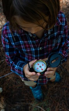 Child in nature looking at a compass clipart