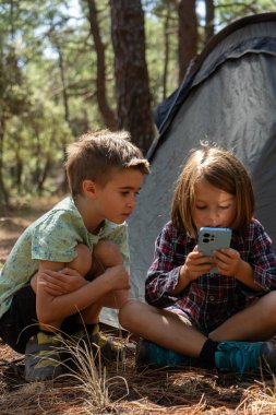 Ormanda kamp yapan iki çocuk akıllı telefonlarına bakıyor.