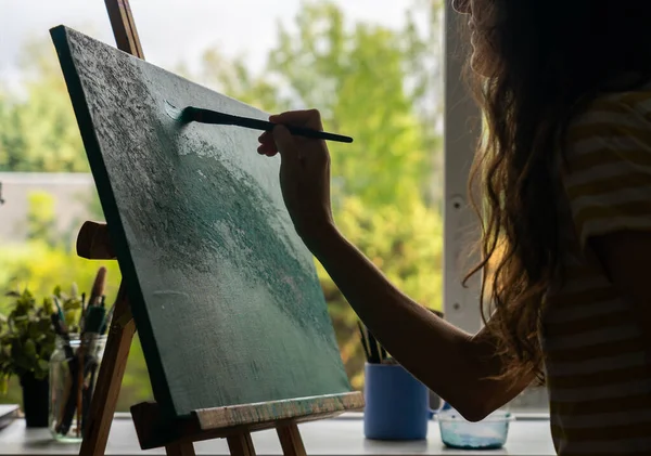 Woman in profile creating an abstract art painting on a canvas on an easel
