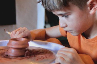 Çocuk çömlekçi çarkında aletlerle kil şekillendiriyor.