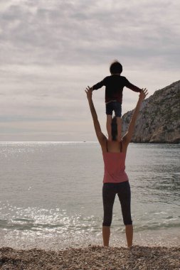 Bir çocuğun silueti annesinin omuzlarında denize bakıyor.