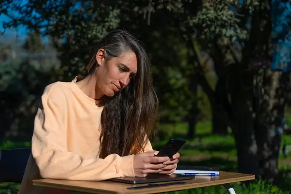 Woman working with cell phone and desk outdoors in peach clothes