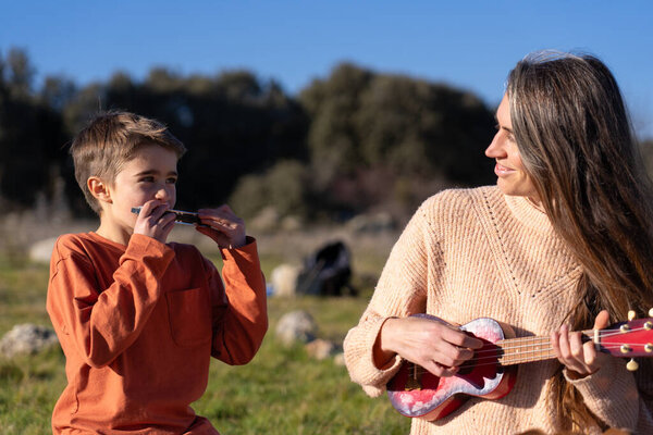 Mother and son playing music in nature. The boy playing the harmonica and the woman playing the ukulele