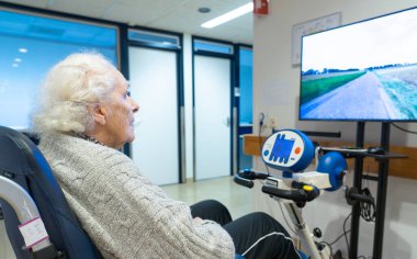 Huzurevinde kıdemli bir kadın bisikletiyle rehabilitasyon yapıyor.