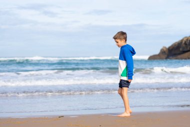 Deniz kıyısındaki yalın ayak çocuk.