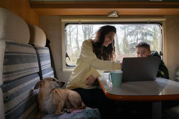 Mother with her son and dog looking at the computer inside a motorhome