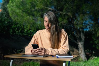 Doğada cep telefonu ve masasıyla çalışan bir kadın.