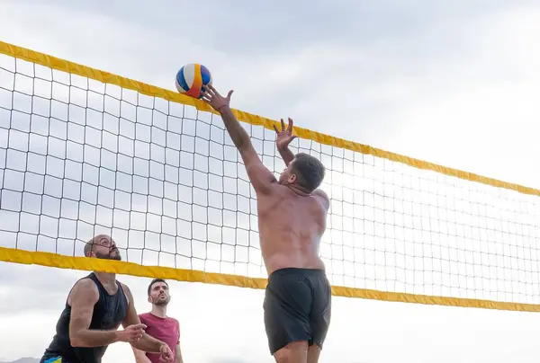 Kumsalda voleybol oynayan adamlar.