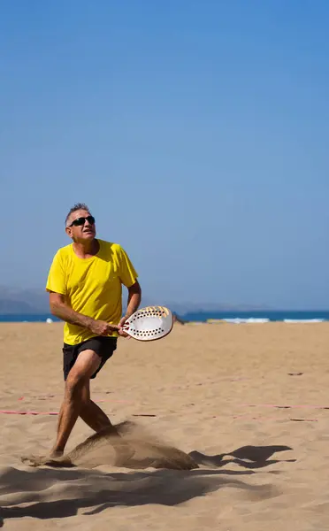Senior man with active lifestyle playing beach tennis on vacation