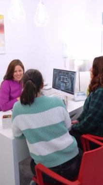 İki kadın dişçi kliniğinde dişçiyle konuşuyor.