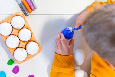 Çocuk yukarıdan görünen bir paskalya yumurtası çiziyor