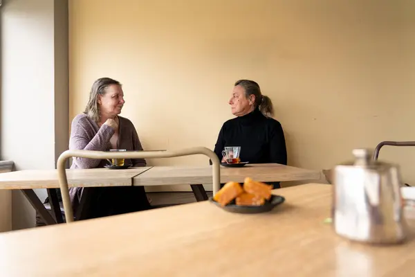 Two 60-year-old women drinking tea in a peach-colored tea shop