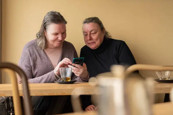 Two older women looking at their cell phones together in a coffee shop