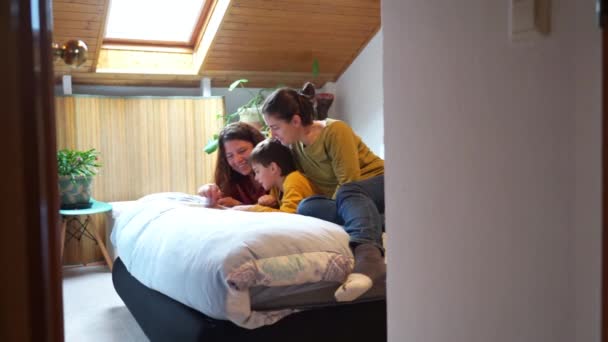 Lgtbiqia 2人の母親と息子の家族は ベッドルームのベッドに家族の写真とアルバムを見ています — ストック動画