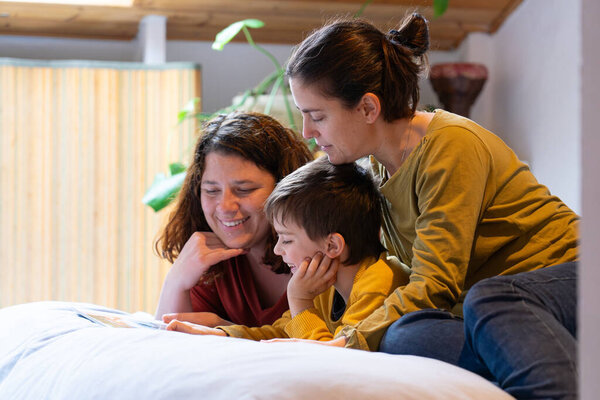 ЛГБТКИЯ + семья из двух матерей и ребенка, которые вместе смотрят фотоальбом дома