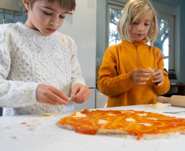 Çocuklar ev yapımı pizzanın malzemelerini koyuyorlar.