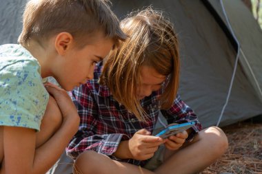 Ormanda kamp yapan çocuklar akıllı telefonlarıyla oynuyorlar.