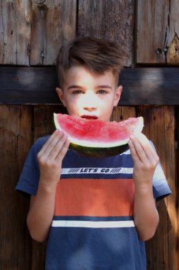Karpuz yiyen çocuk kameraya bakıyor.