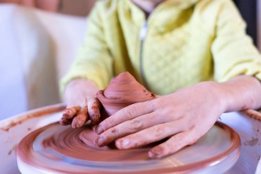 Çocuğun elleri çamurdan tekerlek yapıyor.
