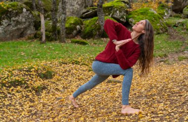 Sonbaharda ormanda yoga yapan orta yaşlı bir kadın.