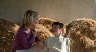 Çiftlikte birbirine gülümseyen samanlarla bakan iki çocuk.