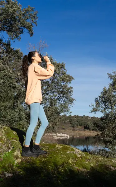 stock image Sporty woman drinking water in nature, wearing a peach colored sweatshirt
