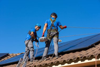 Enerjinin kendine yetmesi için güneş panelleri kuran iki adam.