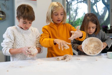 Three children making the dough to make homemade pizza in the kitchen of a house clipart