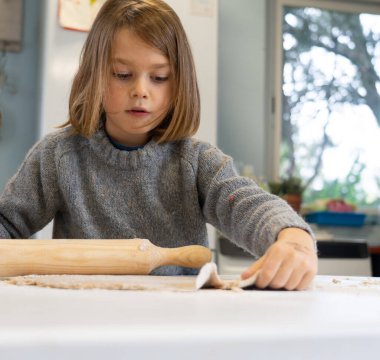 Evdeki mutfakta pizza hamuru yoğuran çocuk.