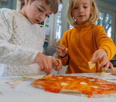 İki kardeş ev yapımı pizzaya malzeme ekliyor.