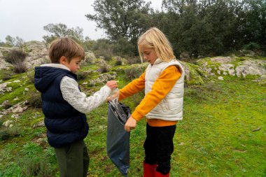 İki çocuk doğadan çöp topluyor.