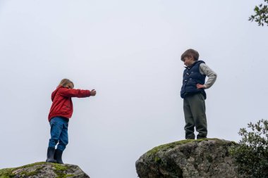 İki çocuk doğada büyük kayalıklarda oynuyor.