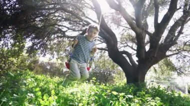 8 yaşındaki beyaz çocuk doğada bir salıncakta sallanıyor.