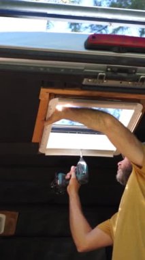Kamp minibüsüne tavan penceresi takan bir adam. Kafkasyalı bir adam karavanda kamp yapıyor.