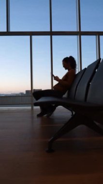Havaalanı kapısında uçağının kalkmasını beklerken cep telefonuna bakan bir kadın.