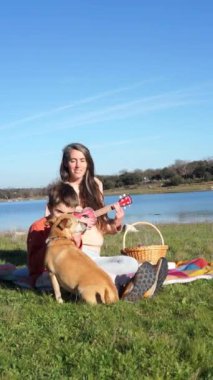 Anne oğul ve köpeğin ailesi doğada ukulele ve mızıka çalıp piknik yapıyorlar.