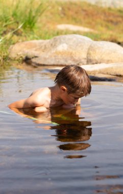 Nehirde yıkanan bir çocuk bir şey arıyor.